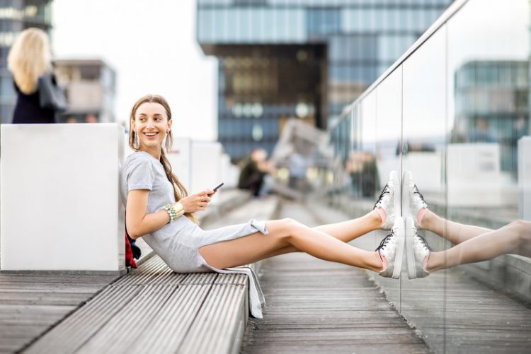 Lifestyle portrait of a business woman dressed casually sitting with phone outdoors at the modern district in Dusseldorf city, Germany